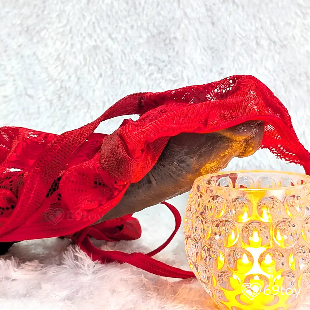 Red lace fabric draped over a black dildo white surface with a yellow candle.