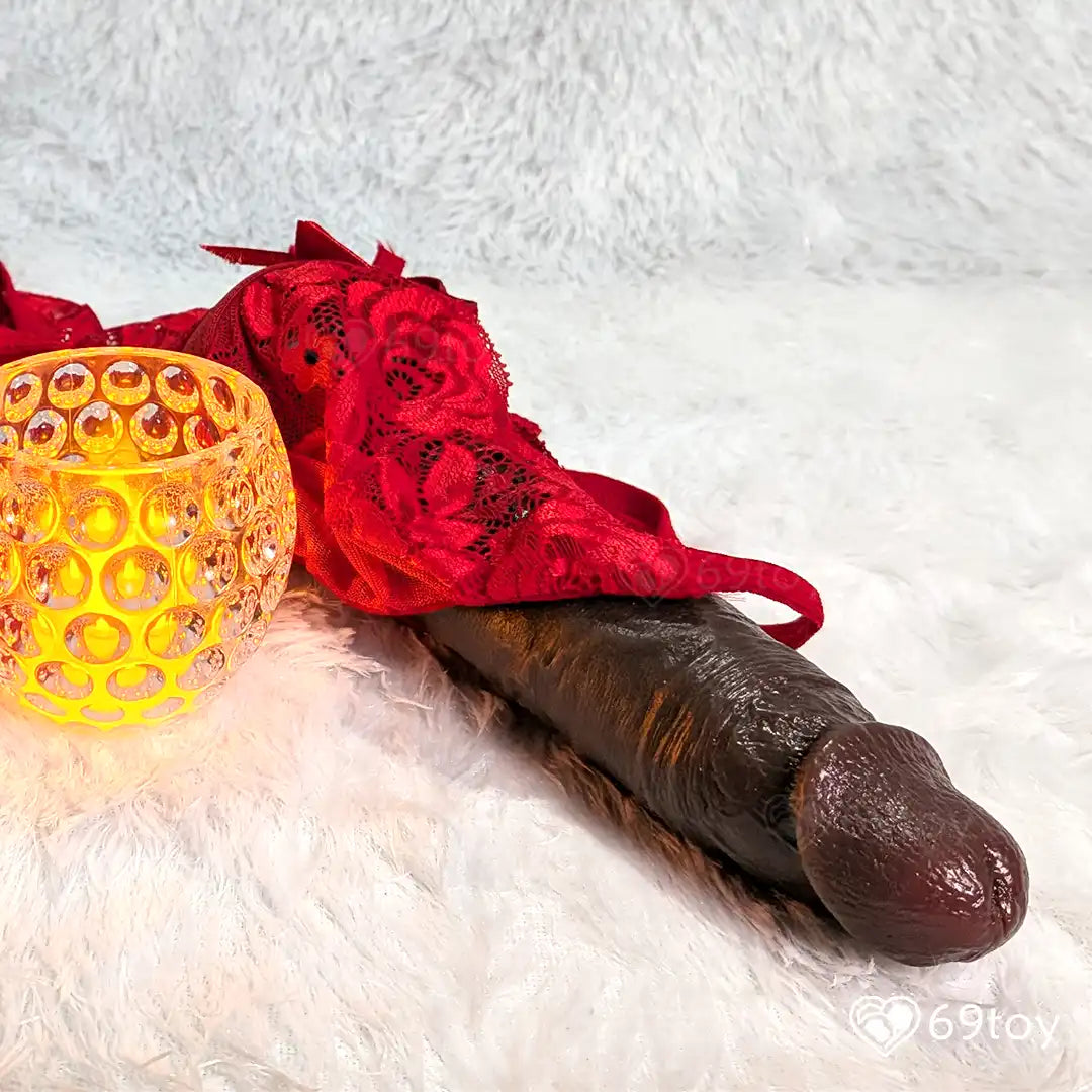 dildo wrapped in red lace on a white surface with a yellow candle.
